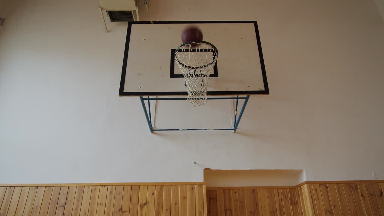 A ball falls through the basketball hoop. Kids are playing in a school gym