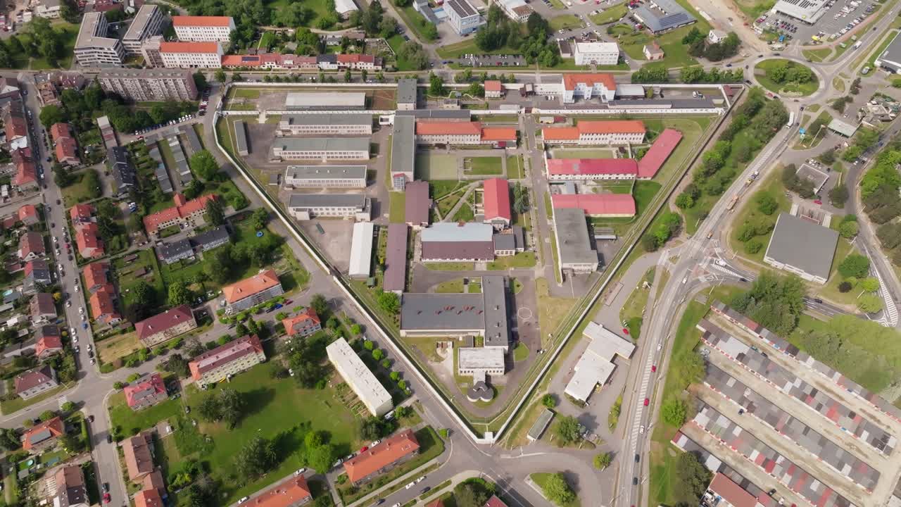High-altitude aerial arc revealing the full prison compound and perimeter defenses; smooth curving motion, continuous shot, daytime