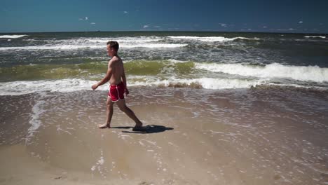 young man in red shorts walks in a beach by the sea
