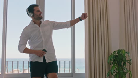 happy travel man dancing in hotel room having fun listening to music celebrating summer vacation enjoying carefree holiday lifestyle wearing headphones