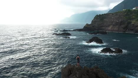 one man standing alone on the edge of a cliff next to the seixal natural pools in madeira