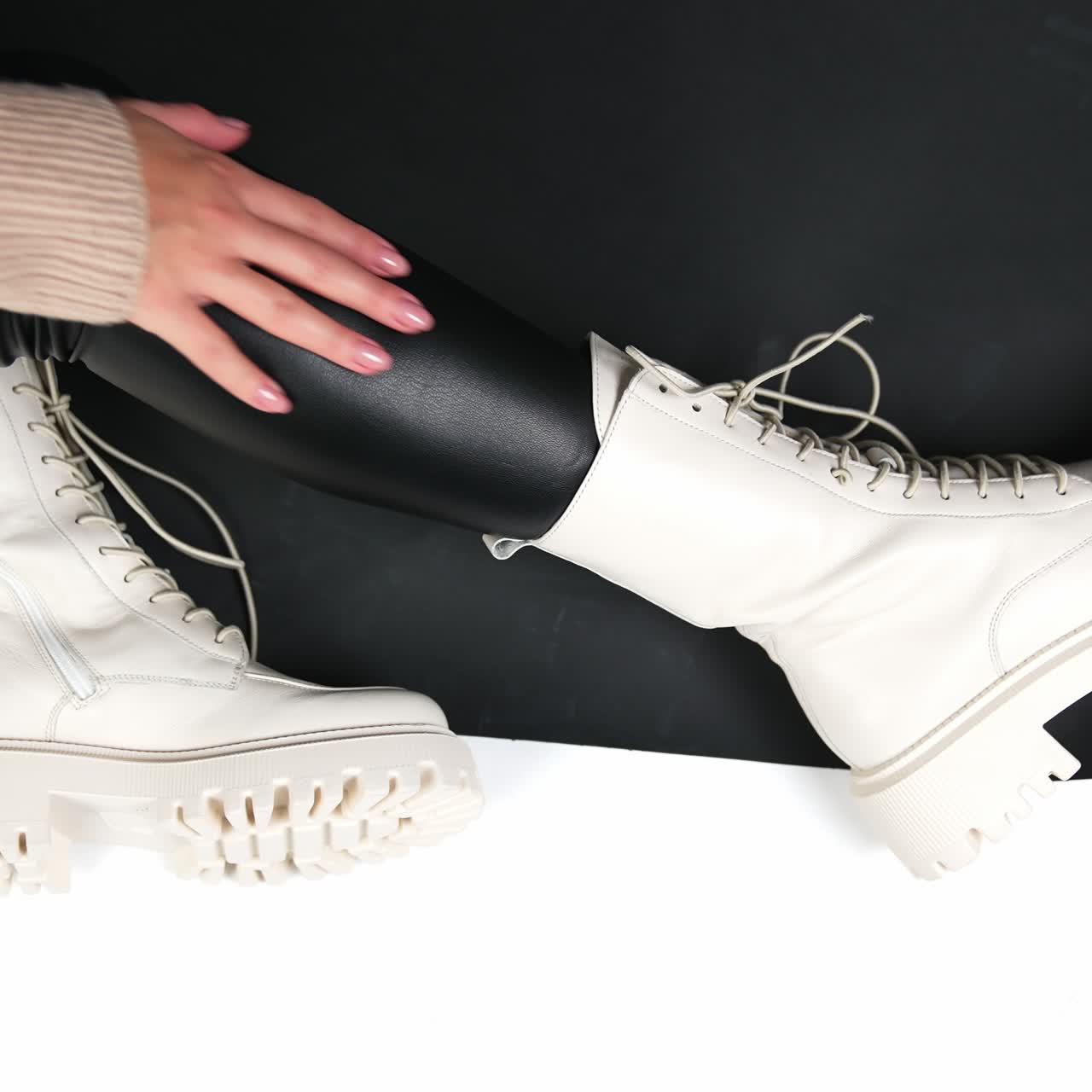 Presentation of milk-white tractor boots with laces. Model sitting in the floor in modern stylish footwear for cold season. Close up
