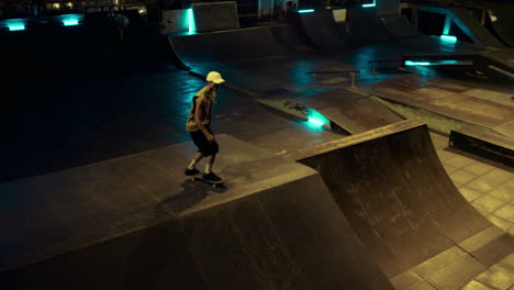 Young-skater-performing-trick-on-skate-board-in-ramp-at-night-skate-park.