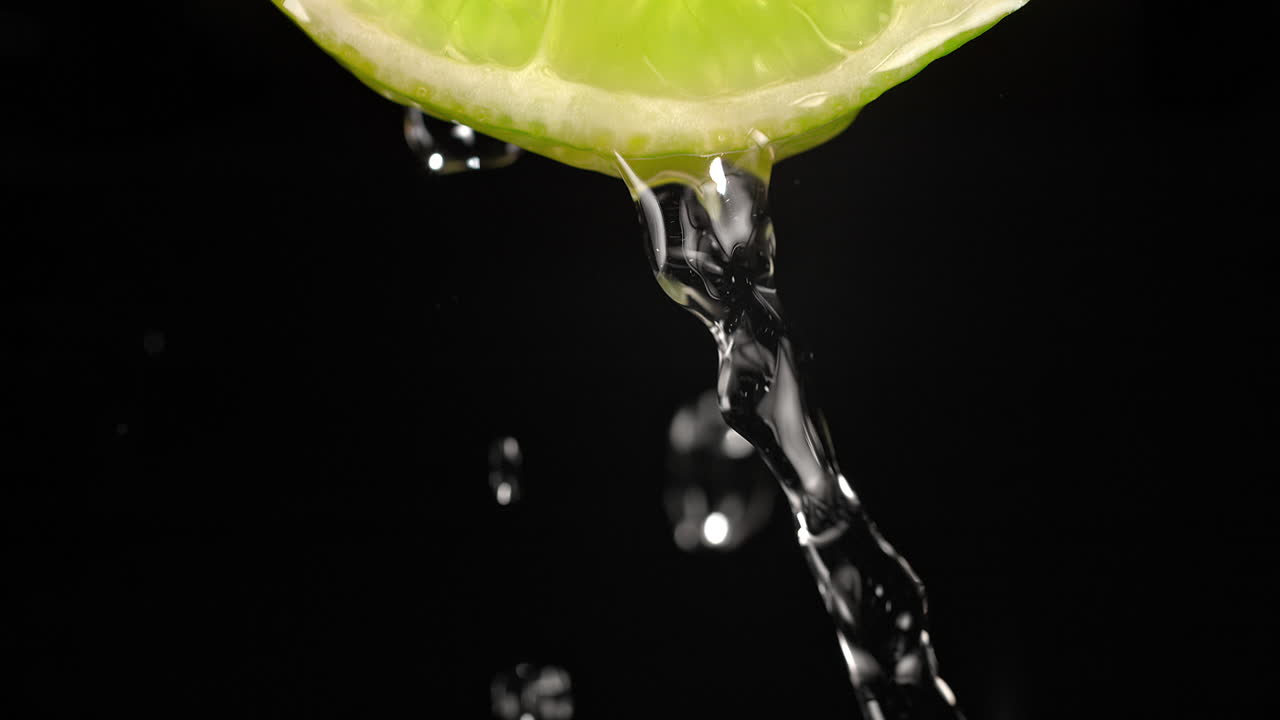 rodaja de cal vertida con agua en cámara lenta y macro sobre un fondo negro