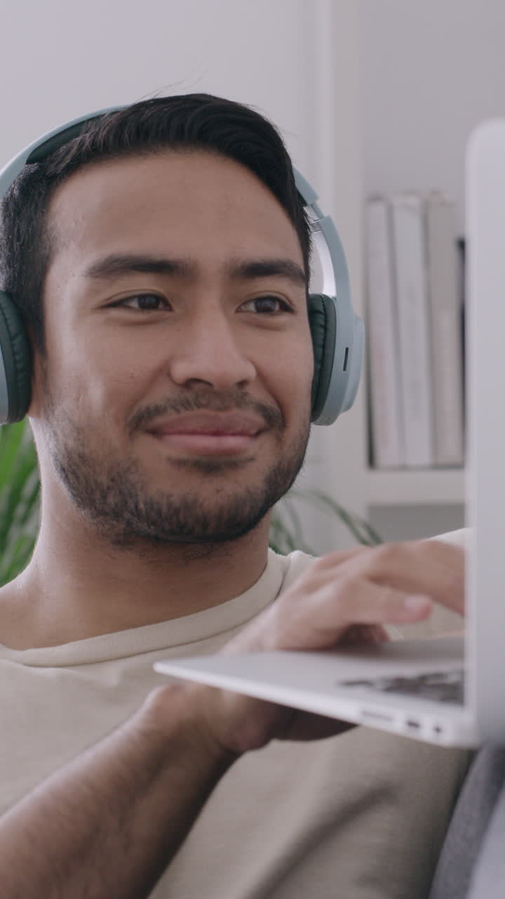 Joven feliz con auriculares usando una laptop y sonriendo
