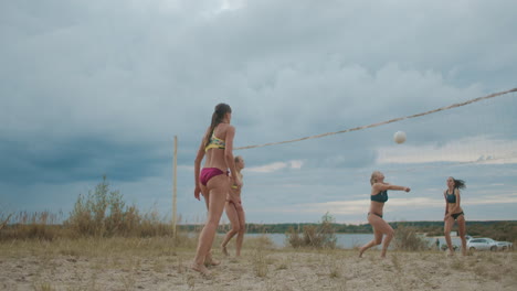 Partido-De-Dos-Equipos-Femeninos-De-Voleibol-De-Playa-En-Un-Día-Nublado-De-Verano,-Las-Mujeres-Pasan-Sirviendo-Pelota-Y-Atacando-El-Campeonato-Amistoso