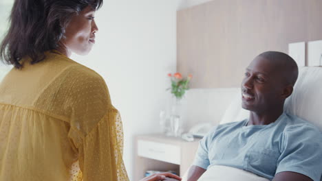 wife visiting and talking with patient husband in hospital bed