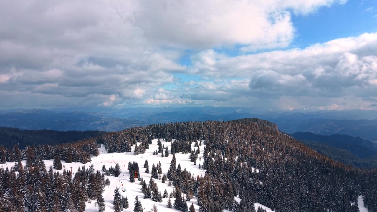 Vinterligt sneklædt bjerglandskab. Høje træer dækket af sne strækker sig hen over bjerget i et vinterlandskab. Skyer fylder himlen over landskabet.