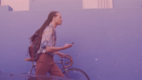 Spots-of-light-against-african-american-man-using-smartphone-while-walking-with-his-bicycle