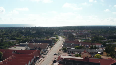 Backwards-fly-street-in-Oksby.-Aerial-view-of-large-buildings-along-road,-shops-and-services-in-small-town-at-sea-coast.-Summer-vacation-destination.-Denmark