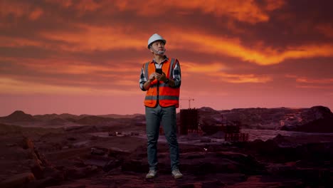 trabajador de la construcción comprobando el teléfono móvil en el sitio de minería al atardecer