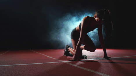 atleta femenina en un fondo oscuro se está preparando para correr el sprint de cross-country desde las almohadillas en la cinta de correr en un fondo oscuro