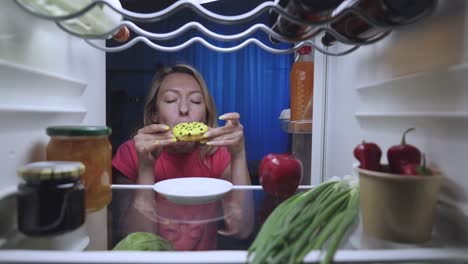 woman eating donut in the refrigerator at night