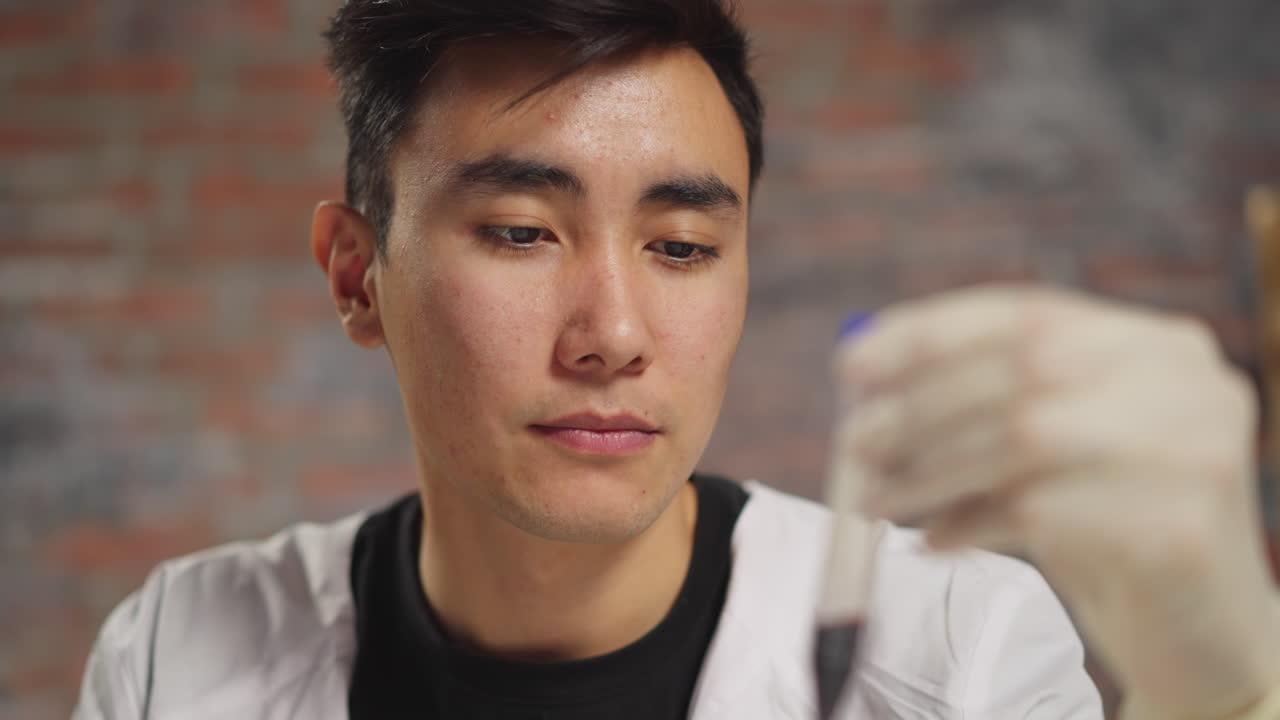 피곤한 아시아 남성 내과 의사가 혈액  ⁇ 플을 가진 튜브를 보고 있습니다.