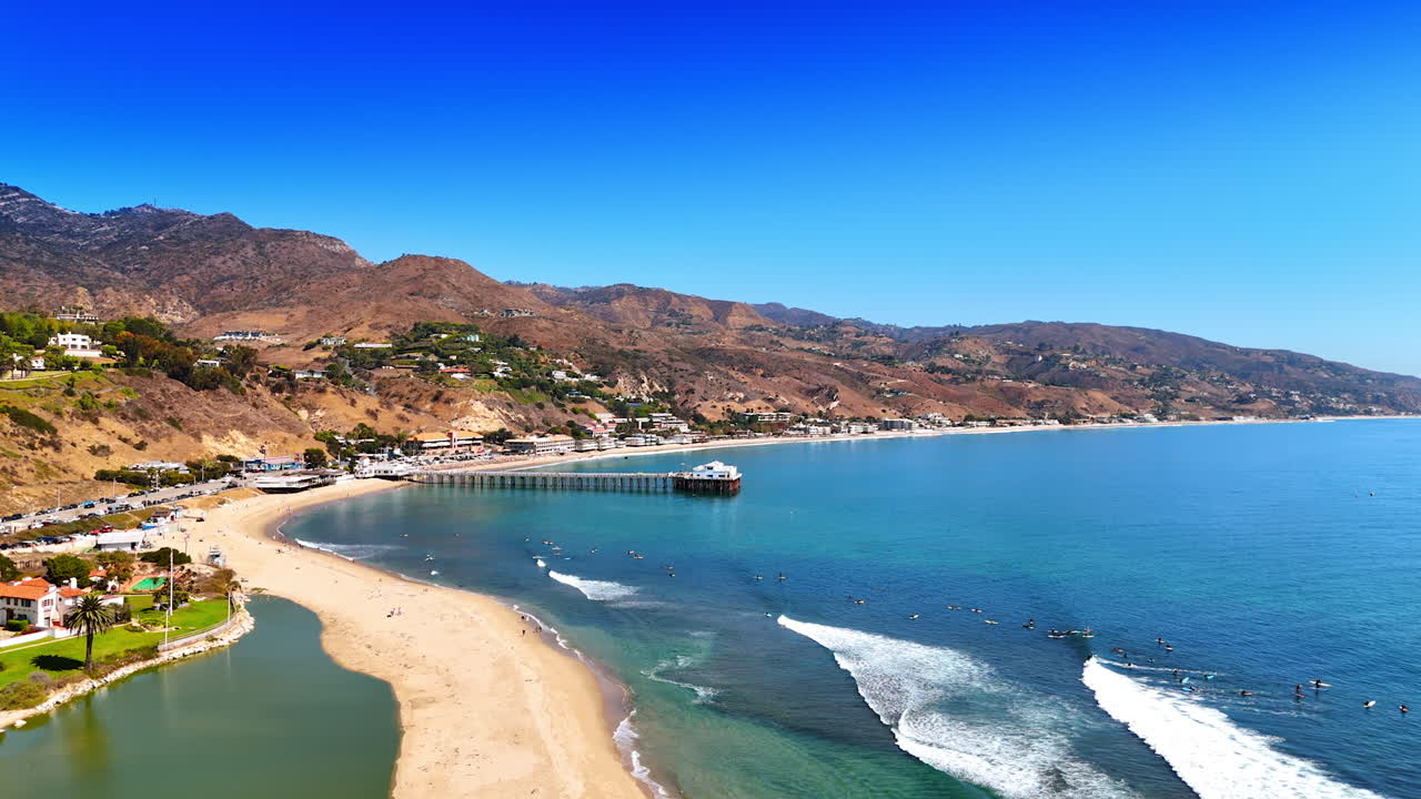 Numerous surfers float on the waterscape waiting for the waves. Surfing in Malibu, Los Angeles County, California, USA. Aerial view