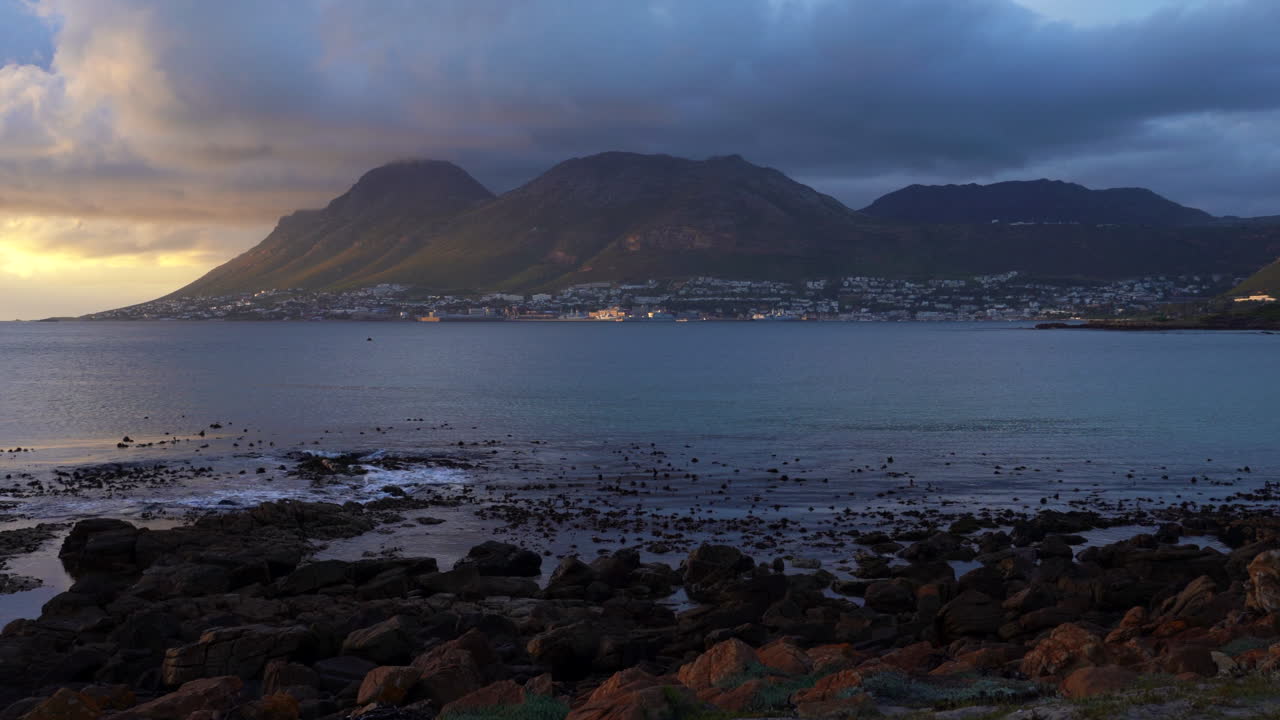 Stunning golden sunrise sunset rain clouds Fish Hoek Simon's Town Muizenberg coastline reef ocean small fishing town on coast Cape Town South Africa Boulder Beach pan down and to the left