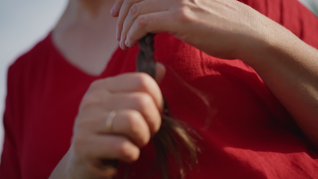 Caucasian woman finishing braided hair outdoors, teacher tucks braid before lesson in sunlit backyard, content expression and tidy long hair with gentle hands completing final touches