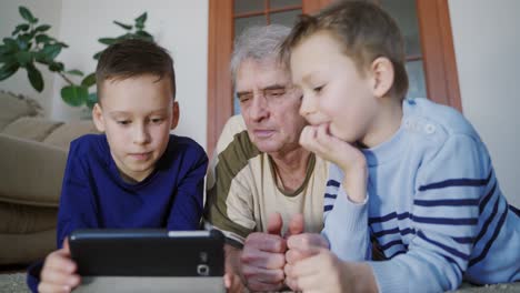 grandchildren teaching to his grandfather to use tablet. home comfort. family idyll.