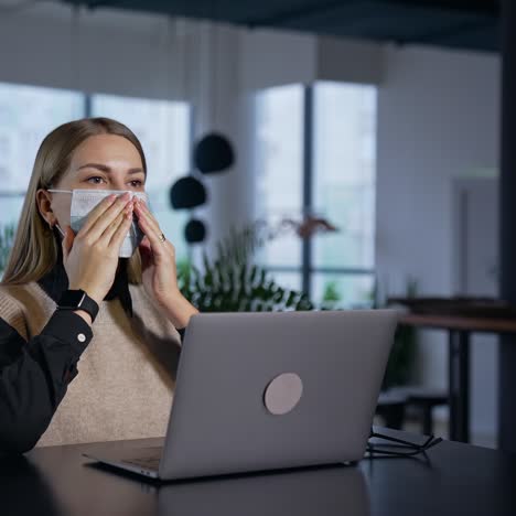 girl in office puts a mask on and fits it to her face. long-haired female employee wears mask and continues her work at the computer
