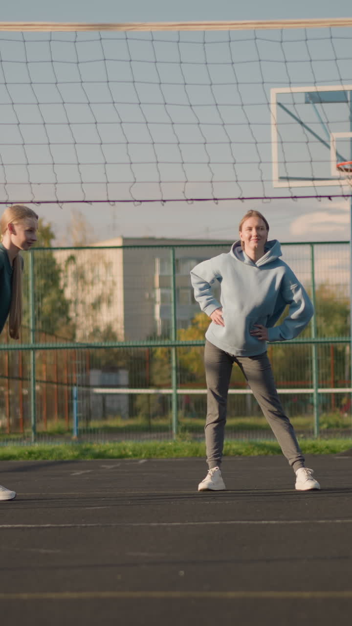 운동복을 입은 스포츠 여성들이 스포츠 경기장에서 야외에서 허리 회전 운동을 수행합니다. 배경에는 배구 코트와 함께 운동 운동을 특징으로하는 활기차고 활기찬 장면입니다.