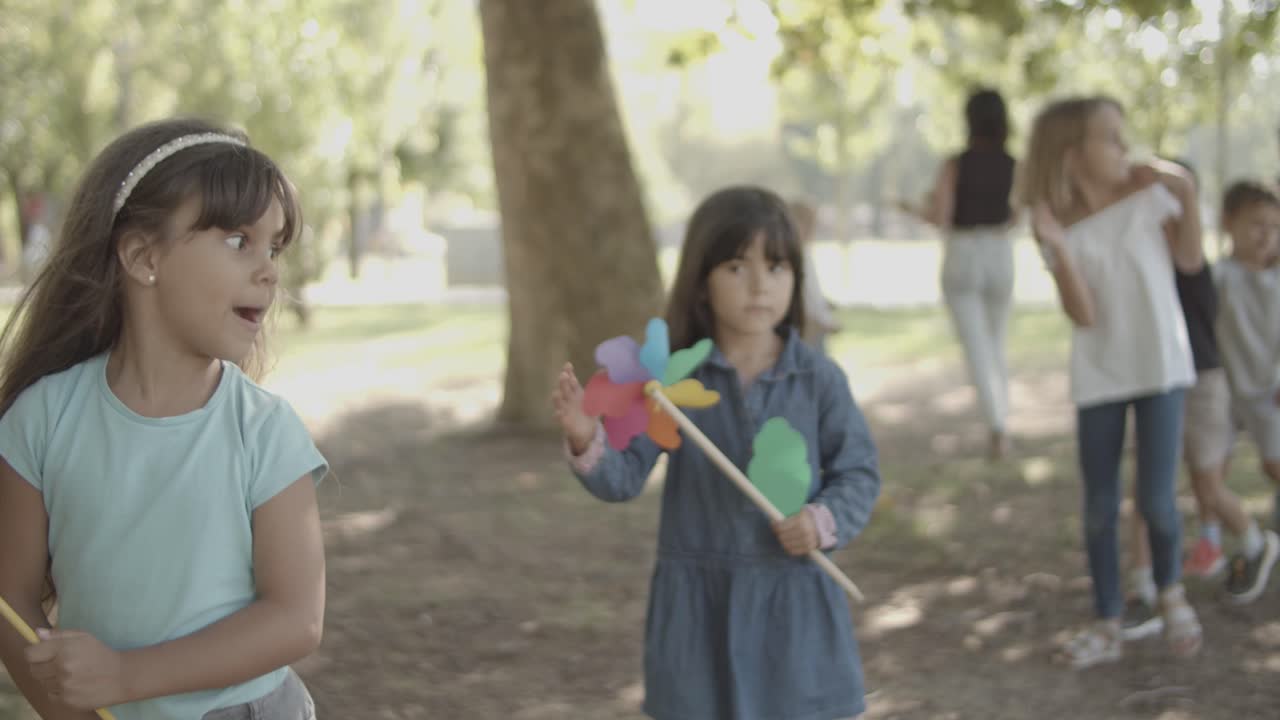 chicas felices sosteniendo abanicos de papel y caminando con amigos en el parque