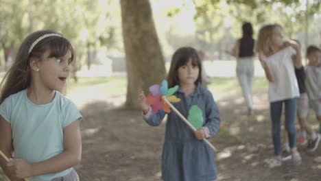 happy girls holding paper fan and walking with friends in the park