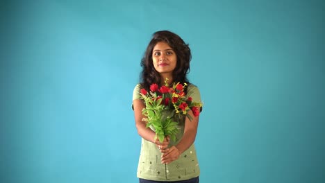 A-young-Indian-girl-in-green-t-shirt-showing-her-bouquet-of-flowers-looking-the-camera-standing-in-an-isolated-blue-background-studio