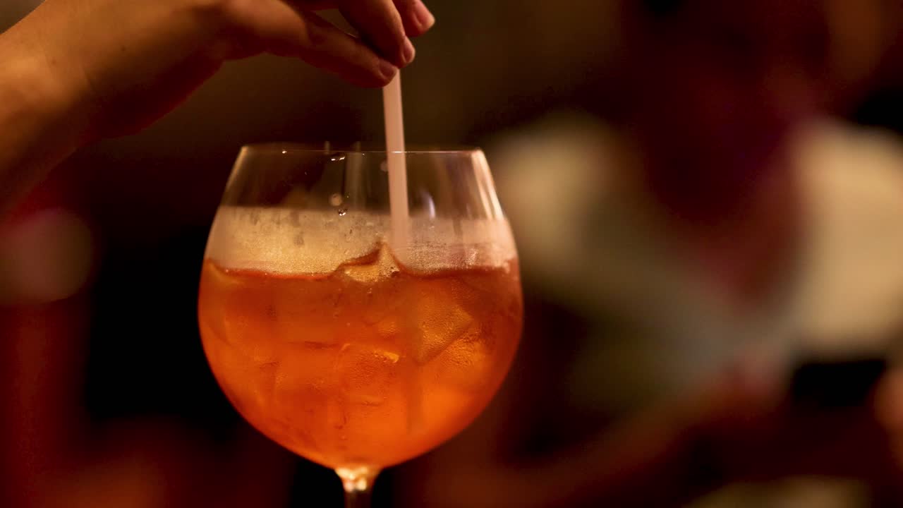 Mano che mescola una bevanda con una cannuccia in un bicchiere