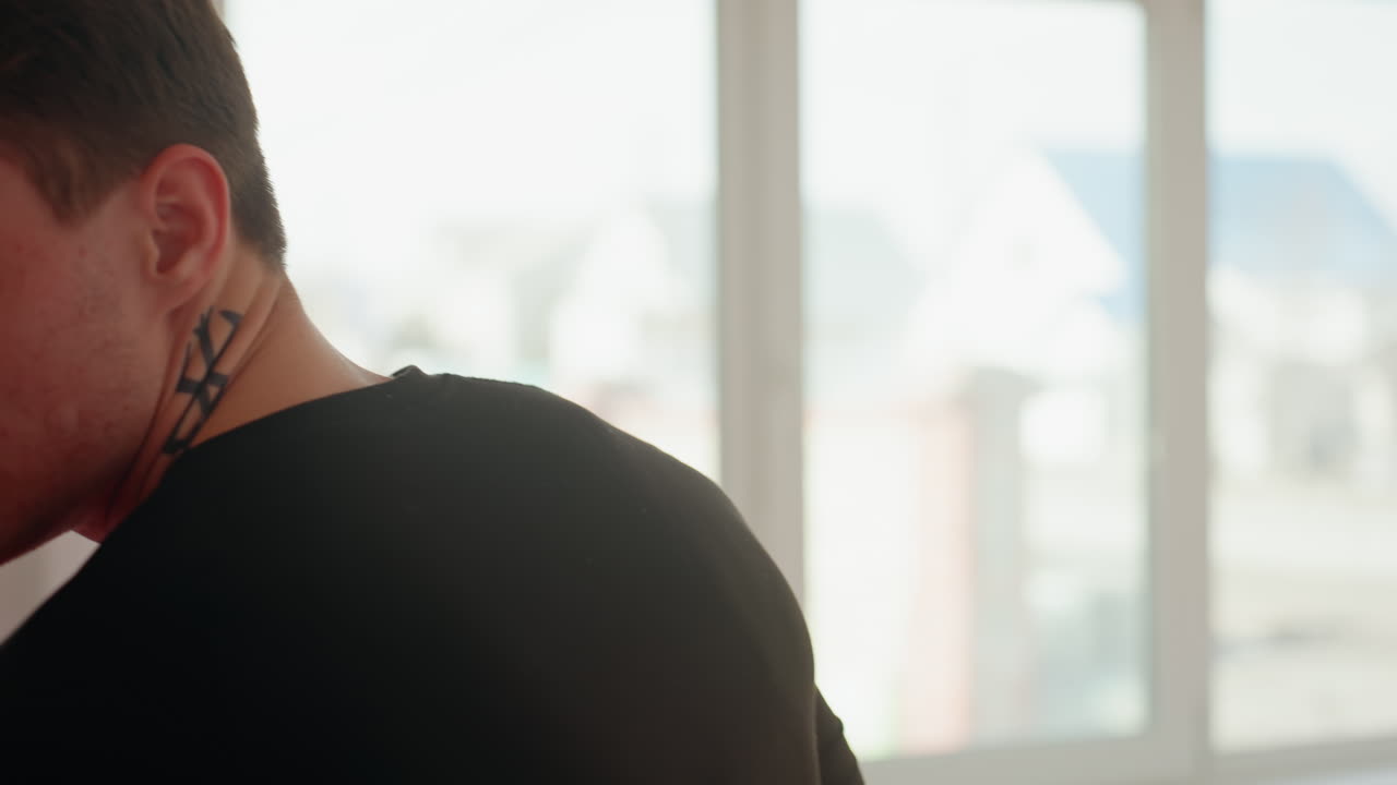 Fighter in black shirt preparing for martial arts sparring, guarded stance with focused expression, hands raised for defense, throwing punches natural light from window highlighting intense concentration