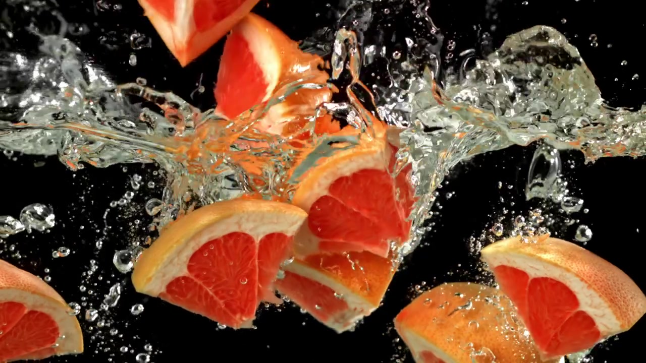 Ferske grapefruktskiver som plasker ned i klart vann i sakte film