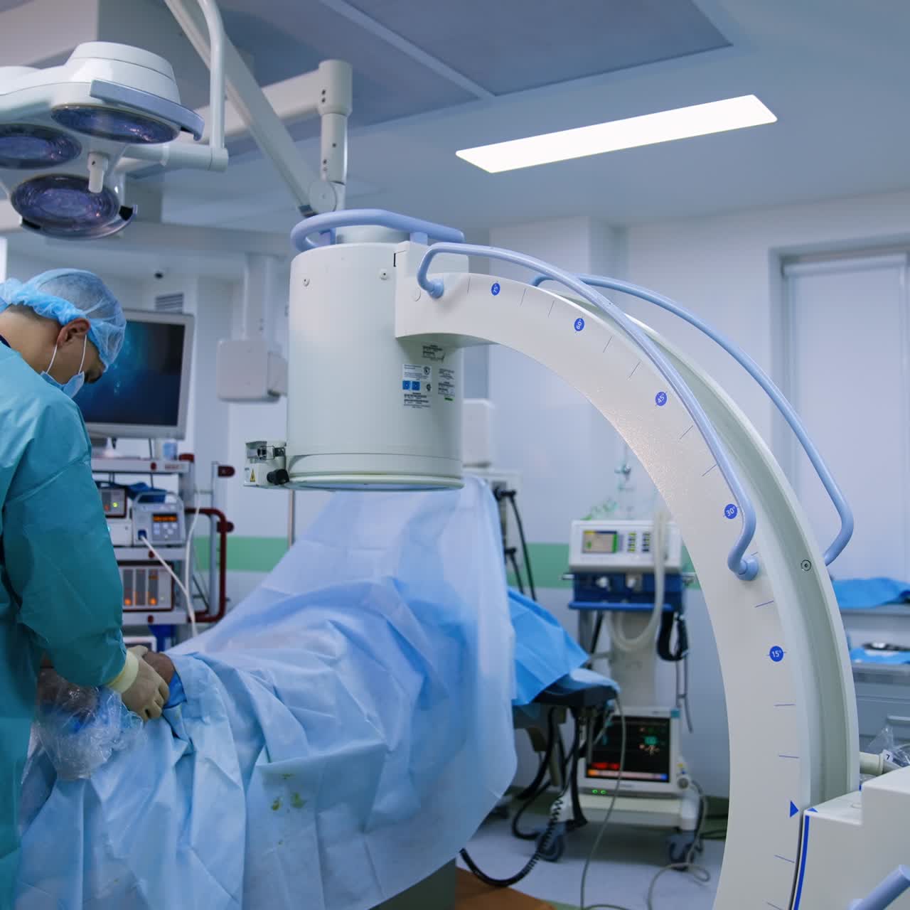 C-arm medical equipment is moved closer to the patient. Assistant preparing patient's foot for x-ray imaging