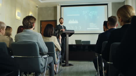 camera zoom out on caucasian businessman talking on a podium in a conference room and showing some charts and graphics on the big screen