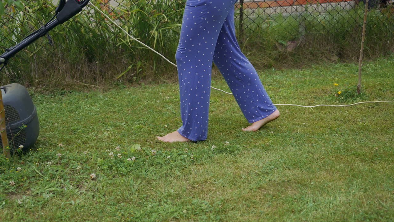 Mowing a lawn with an electric mower. Legs of young woman mowing lawn by lawn mower near country house