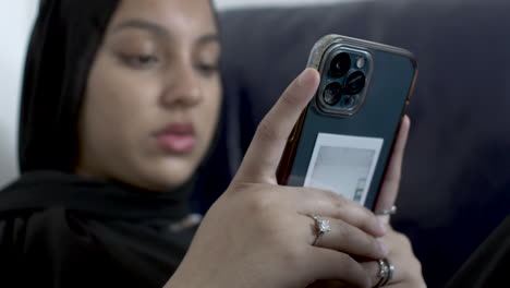 blurred view of young muslim women wearing hijab typing on smartphone whilst sat on sofa