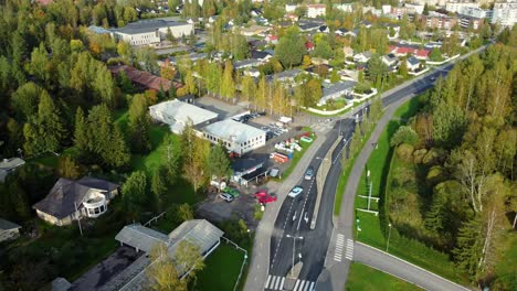 Vista-Aérea-De-Un-Par-De-Autos-Clásicos-Y-Llamativos-Que-Ingresan-A-Un-Estacionamiento-En-Un-Pueblo-Rural-En-Un-Soleado-Día-De-Primavera,-Kerava-En-Finlandia