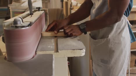 Mid-section-of-african-american-male-carpenter-using-belt-sander-machine-to-polish-wood