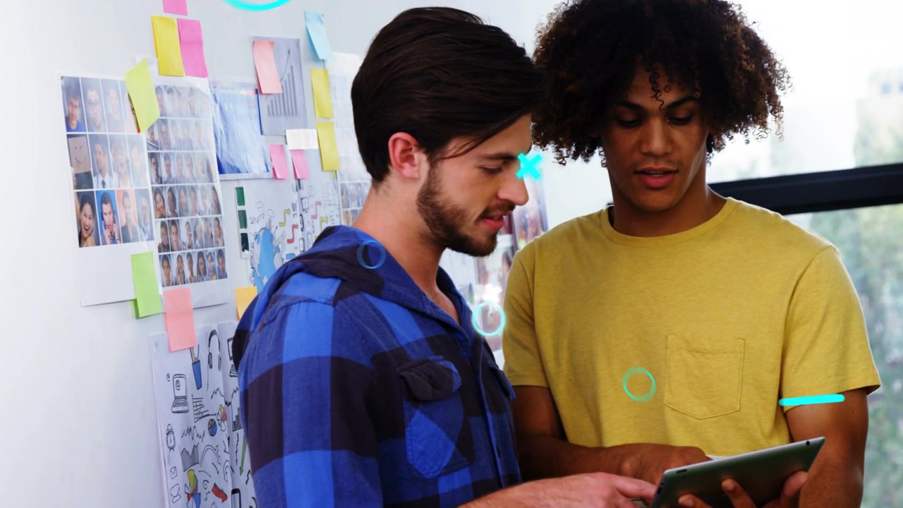 Two men leaning over tablet left man tapping showing overlays while reviewing creative moodboard