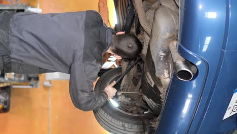 mechanic working on the underside of a lifted blue car in a garage