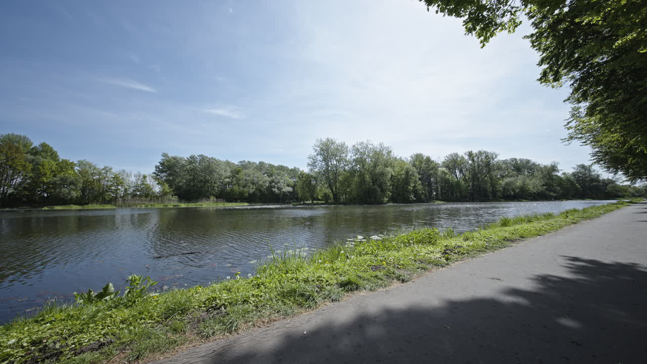 A peaceful riverside view with a walking path surrounded by green trees and blue skies