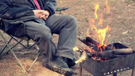 Man-sitting-on-camp-chair-near-bonfire.-Outdoor-recreation.-Campfire-in-forest