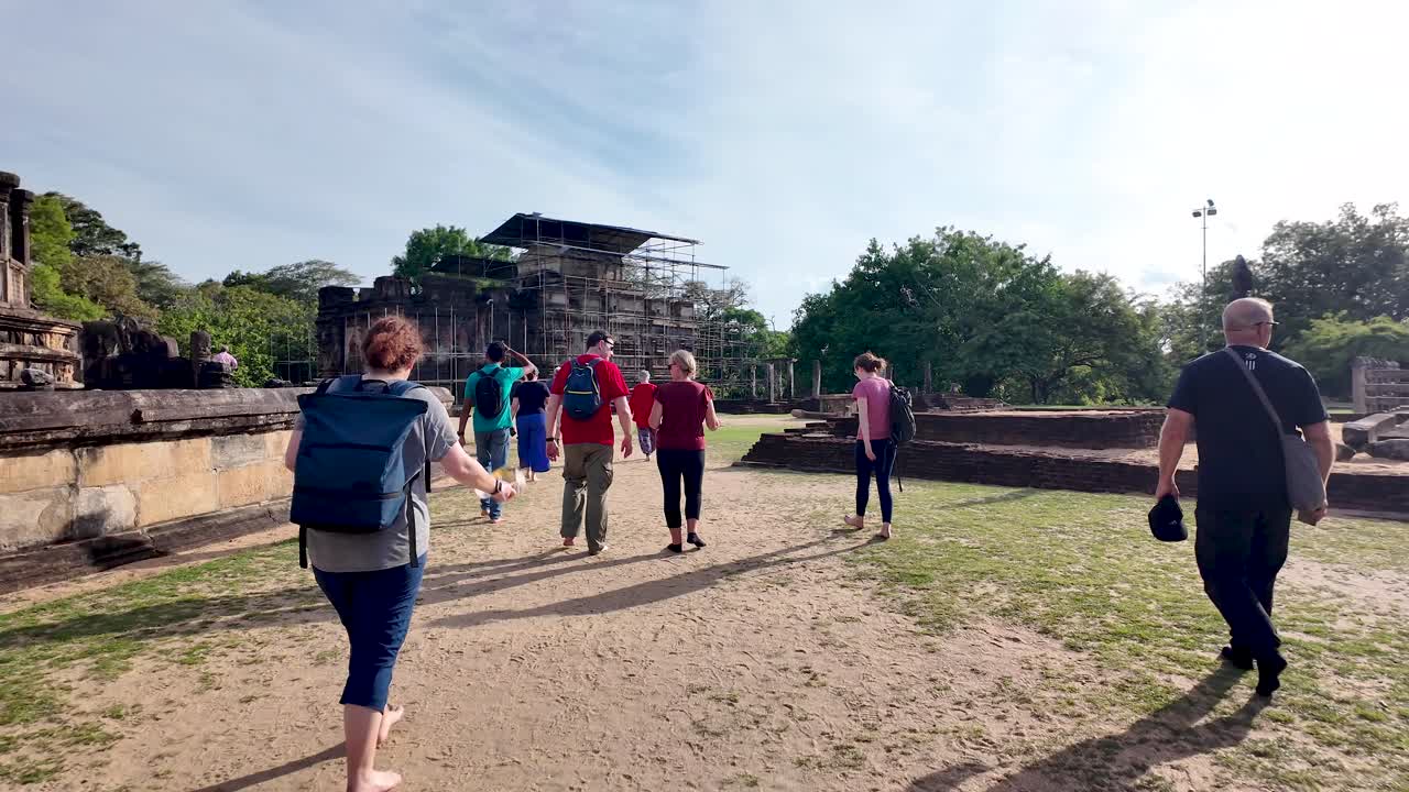 Group of tourists leisurely walks towards scaffolded thuparamaya temple, enjoying the warm sunny weather.