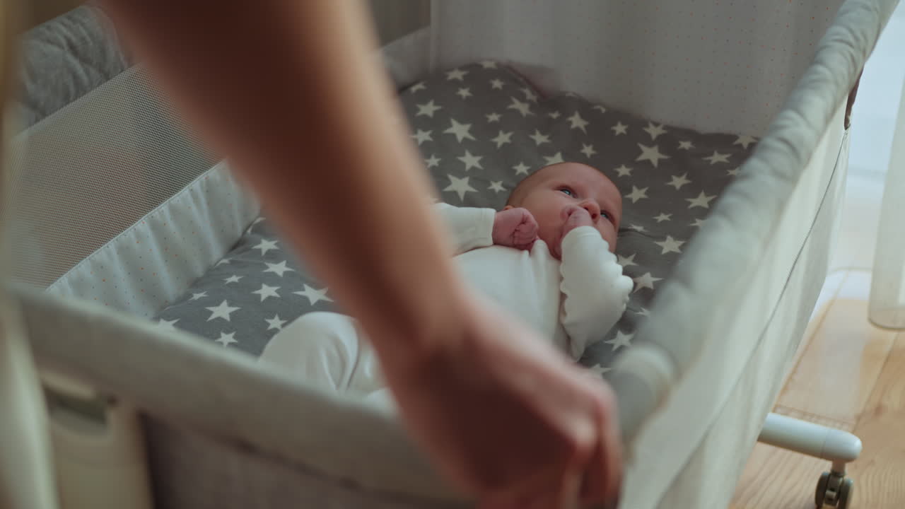 Primo piano di un neonato sdraiato in una culla con lenzuola a stelle, la mano del genitore tocca delicatamente il bambino favorendo il comfort.