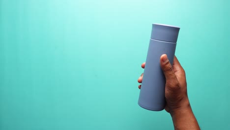 hand holding a blue insulated bottle against a turquoise background