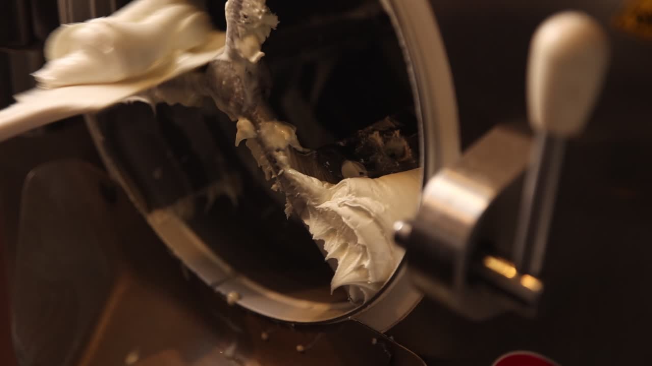 Mano che raschia dessert cremoso da un mantecatore per gelato