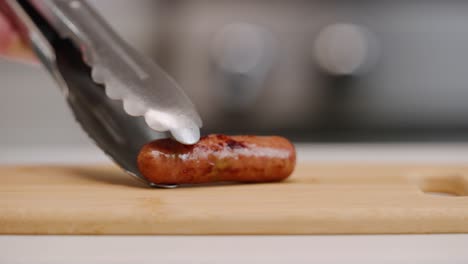 setting a single sausage link down onto cutting board for breakfast with tongs in bright kitchen shallow focus slow motion 4k