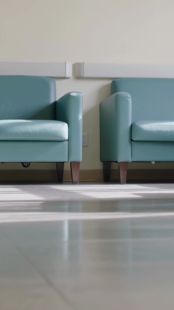 Video verticale: Telecamera che si inclina rivelando sedie color verde acqua in una clinica, documentando una presa elettrica e la luce del sole.