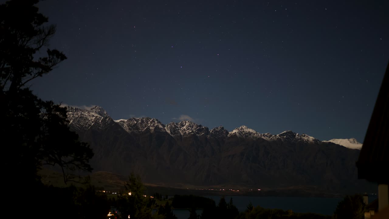 A serene night view of snow-capped mountains under a starry sky in Queenstown, New Zealand