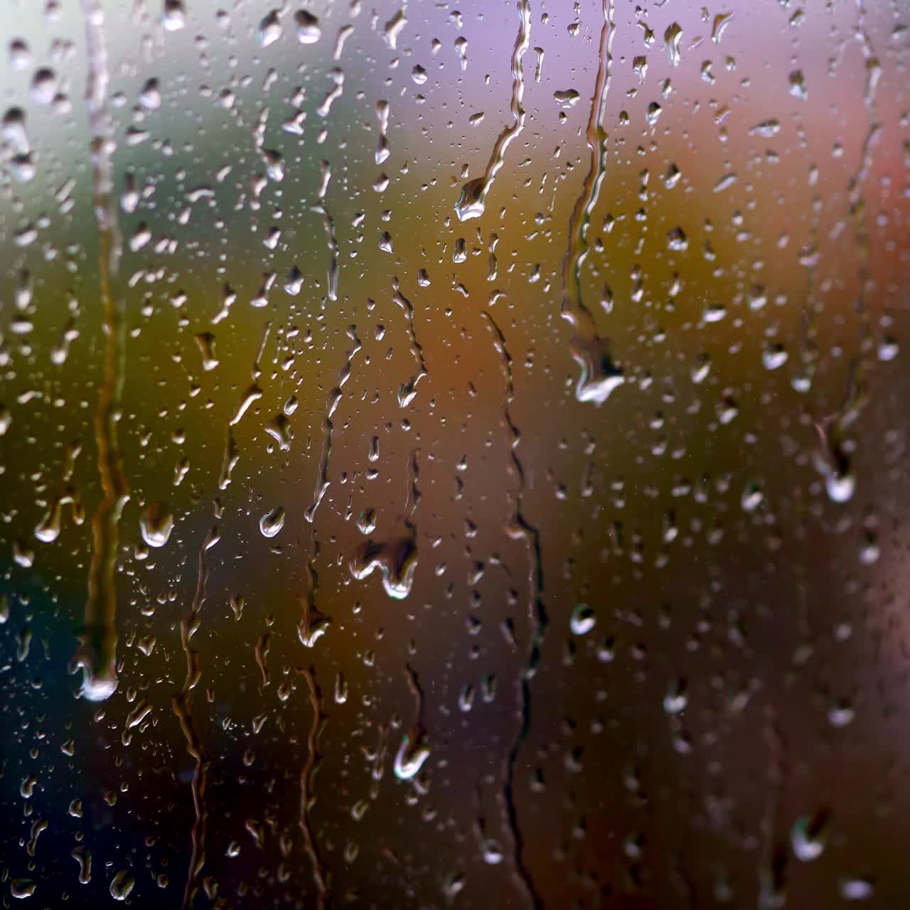 Heavy rain falling outside the window. Big drops moving down on glass background. Texture of flowing droplets on window. Close-up.