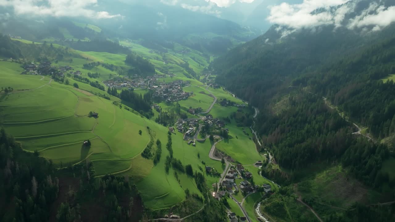 una vista aérea inclinada hacia abajo del valle del pequeño pueblo de la val, tirol del sur, italia con sus sinuosas carreteras que cortan a través de las empinadas colinas cubiertas de hierba