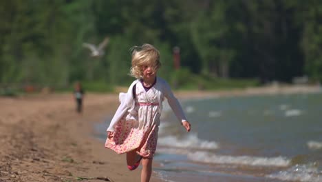 cute little blonde girl running on beach in slow motion splashing in the waves